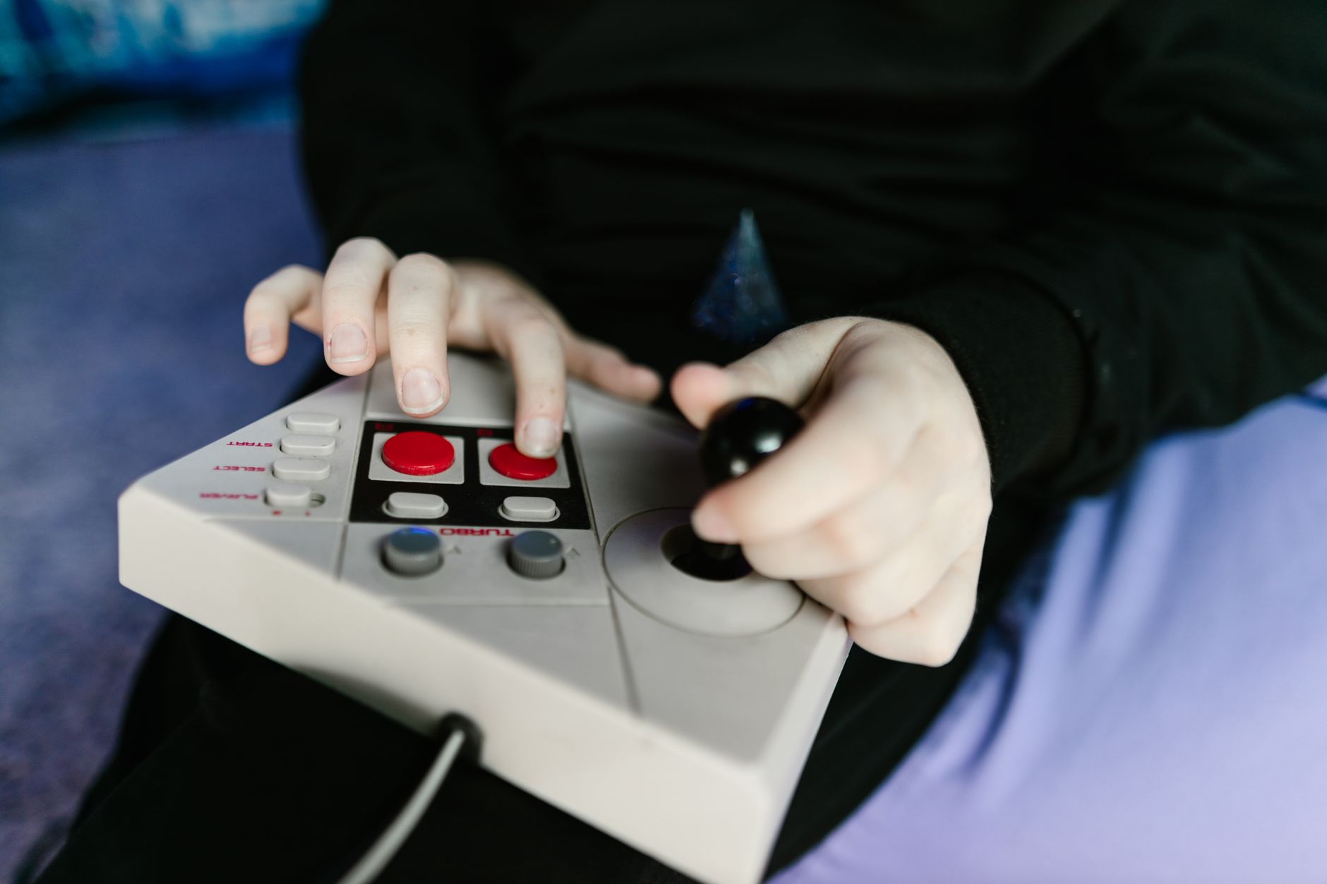 Gros plan sur les mains d’une personne manipulant une manette de jeu d’arcade rétro avec joystick et boutons.