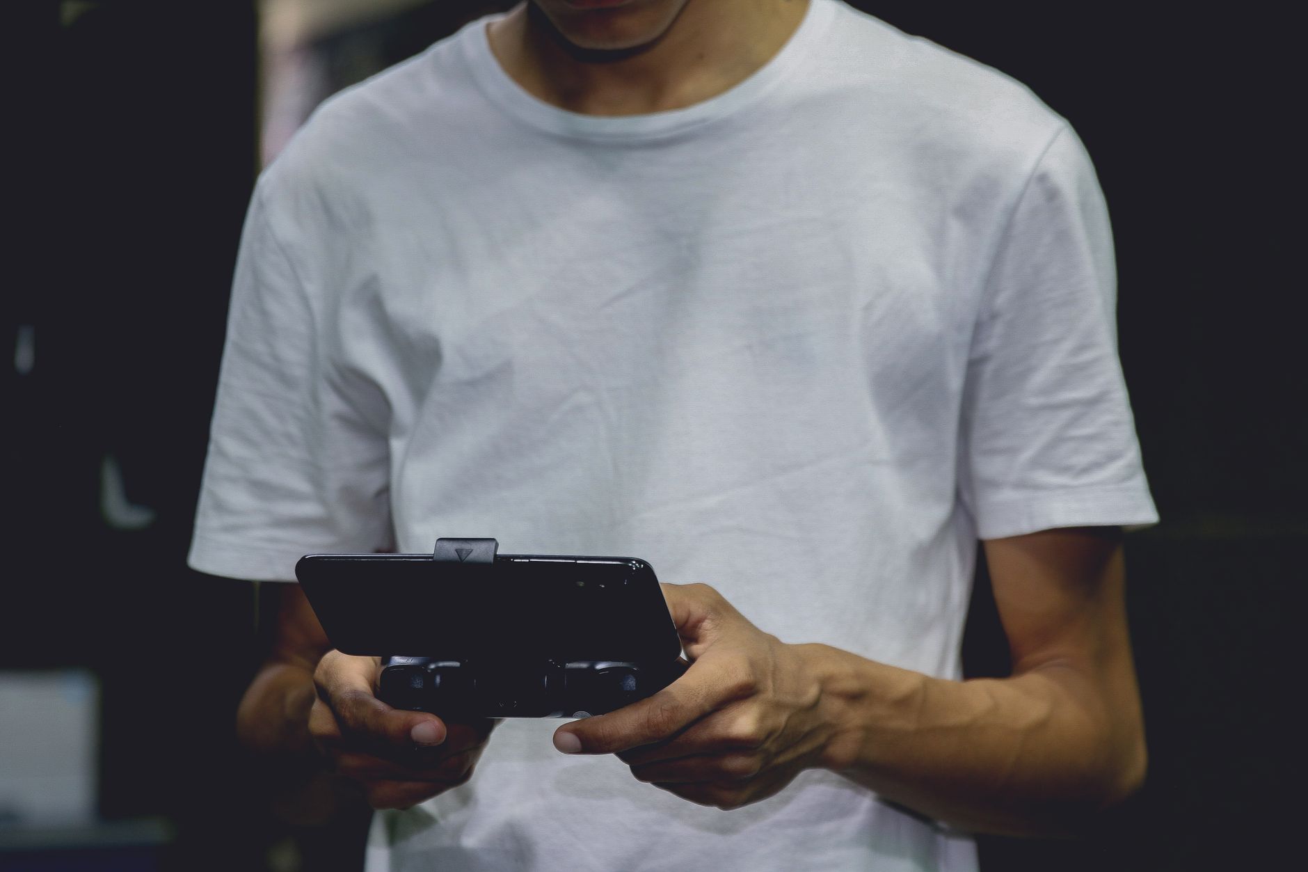Joueur en tee-shirt blanc tenant une manette de jeu pour smartphone à deux mains