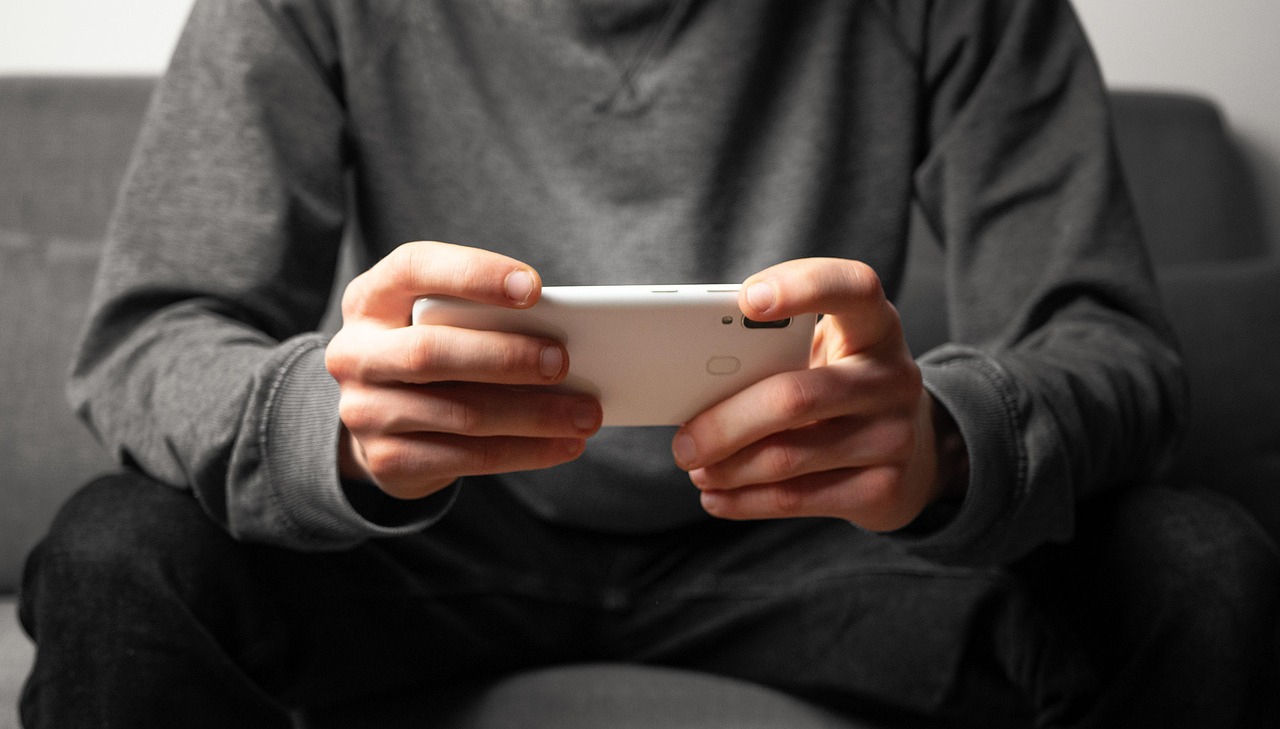 Un homme assis joue à un jeu sur son téléphone tenu à deux mains, photo en noir et blanc