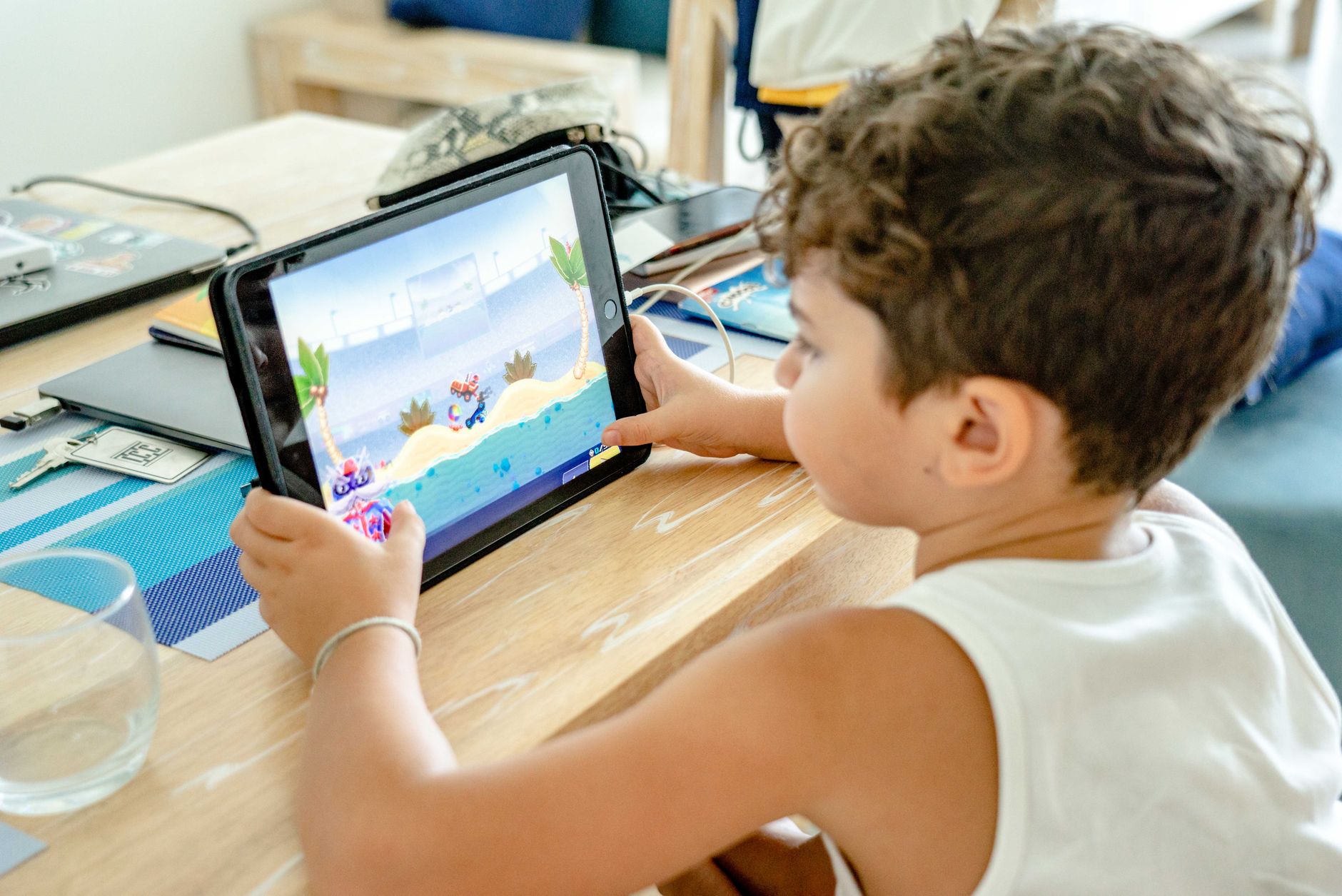 Un jeune enfant joue à un jeu coloré sur une tablette tactile posée sur une table en bois, dans un intérieur.